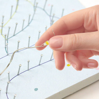 Close-up of colorful strings wrapped around pins creating luminous pattern